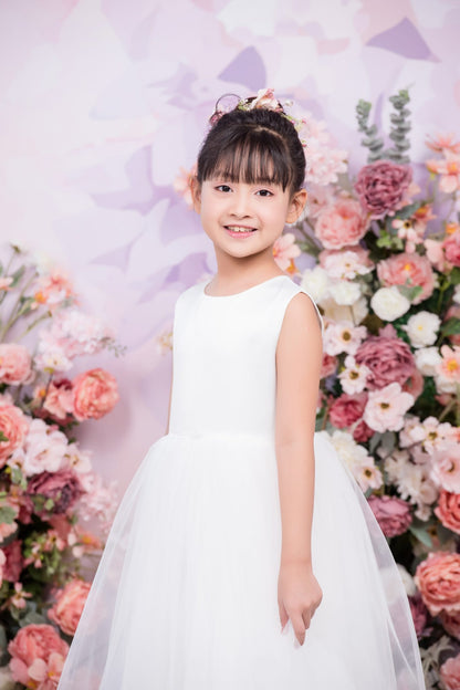 Young girl in a white dress standing in front of a floral backdrop