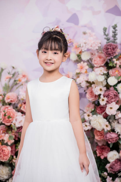 Young girl in a white dress standing in front of a floral backdrop