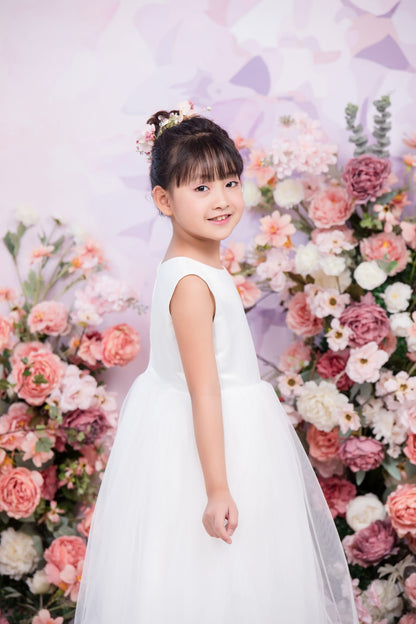 Young girl in a white dress standing in front of a floral backdrop