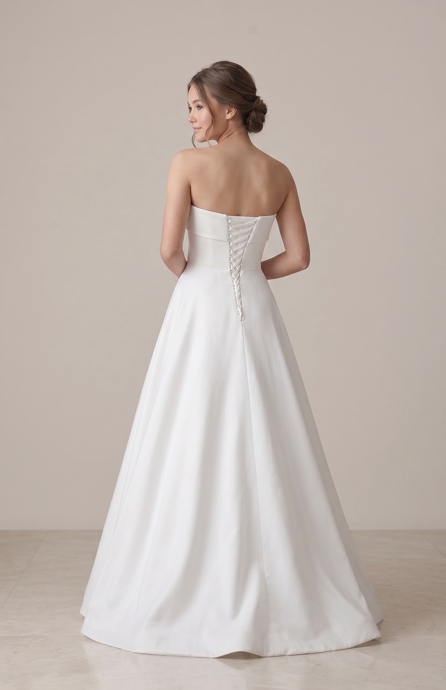 Woman wearing a strapless white wedding dress against a plain background