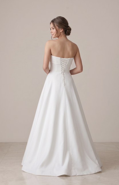 Woman wearing a strapless white wedding dress against a plain background