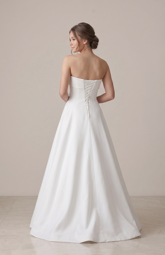 Woman wearing a strapless white wedding dress against a plain background