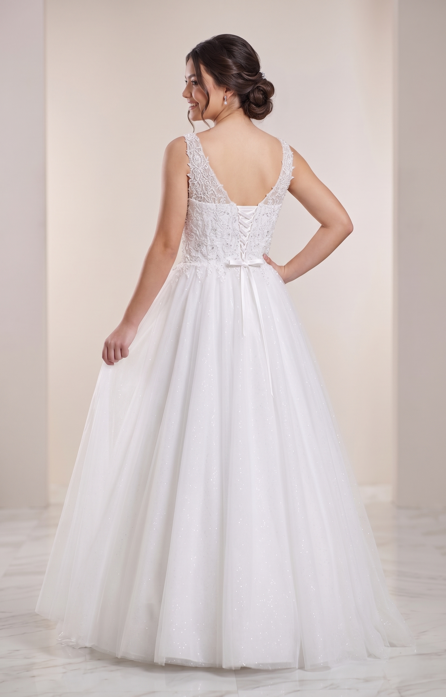 Woman wearing a white wedding dress with a lace bodice and flowing skirt against a plain background