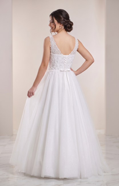 Woman wearing a white wedding dress with a lace bodice and flowing skirt against a plain background