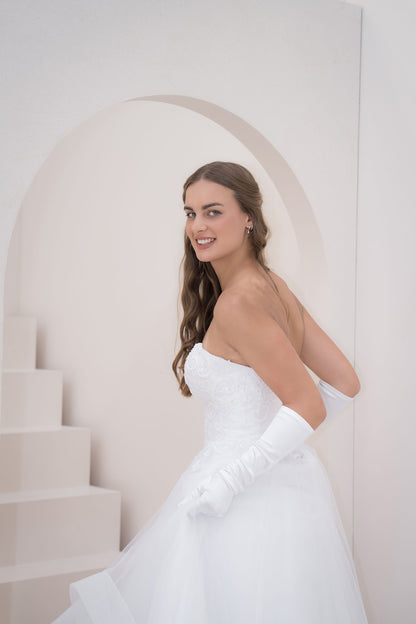 Woman in a white wedding dress standing in a minimalist setting with a white arch and steps.