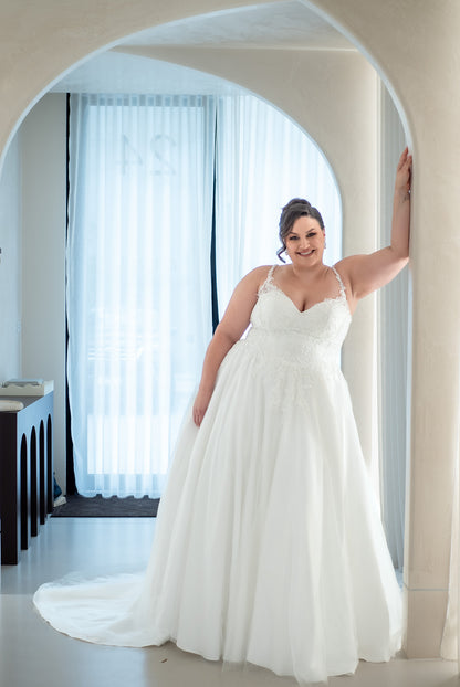 Woman in a white wedding dress standing in a room with large windows.