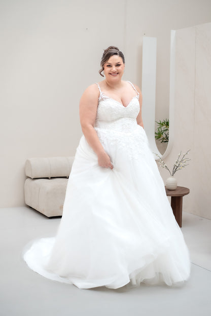 Woman in a white wedding dress standing in a room with a couch and mirror.