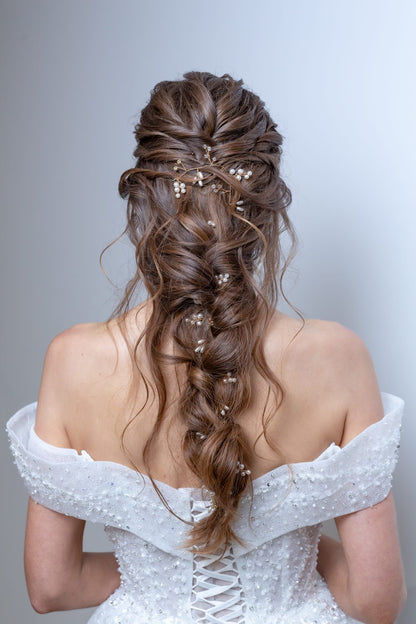 Woman wearing an off-shoulder white dress with intricate hair styling against a light gray background