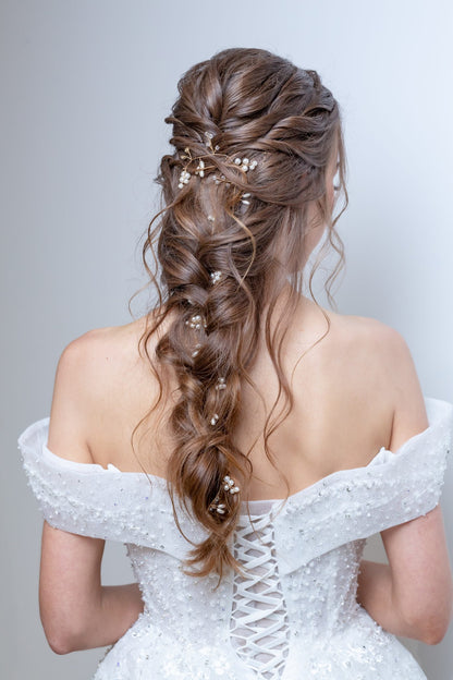 Woman in a white off-shoulder dress with intricate hair styling against a light gray background