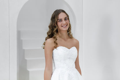 Woman in a white wedding dress standing in front of a white archway.