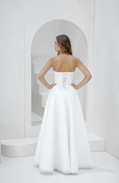 Woman wearing a white strapless gown with a corset back in a minimalistic setting.