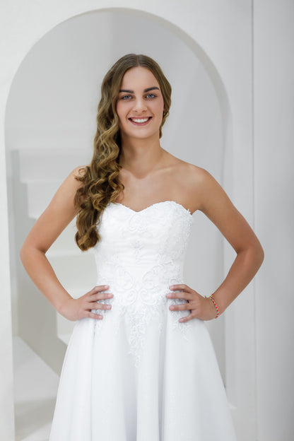 Woman wearing a white strapless dress standing in a white archway.