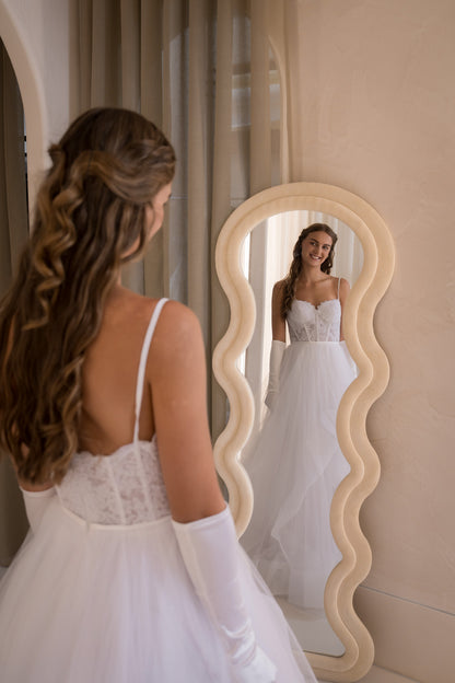 Woman in a white wedding dress looking at herself in a decorative mirror.