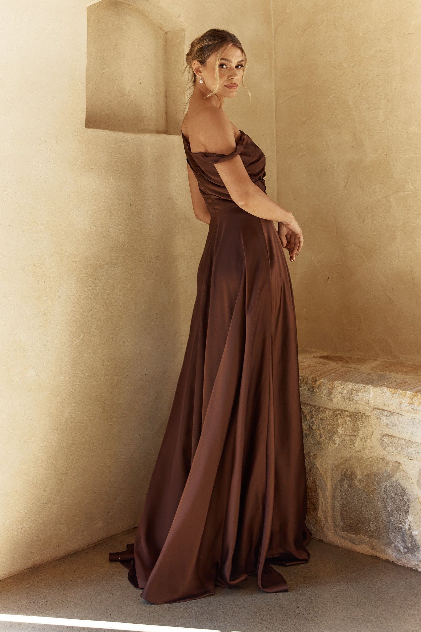 Woman in a brown evening gown standing against a beige wall.