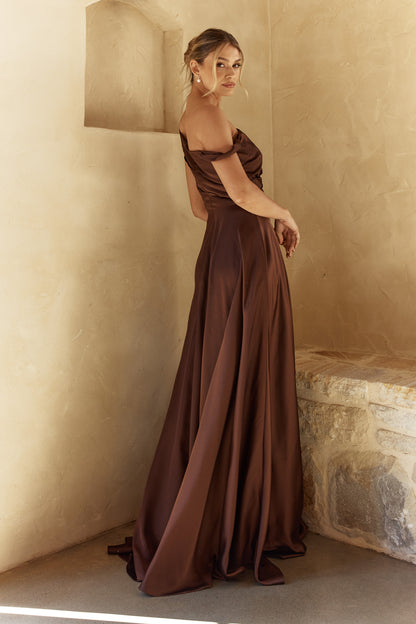 Woman in a brown evening gown standing against a beige wall.