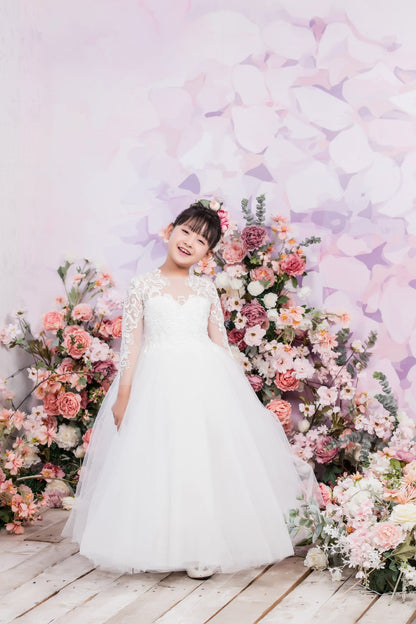 Young girl in a white dress standing in front of a floral arrangement with a butterfly-themed backdrop.