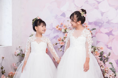 Two young girls in white dresses standing in front of a floral and butterfly backdrop.