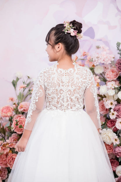 Young girl in a white lace dress standing in front of a floral backdrop