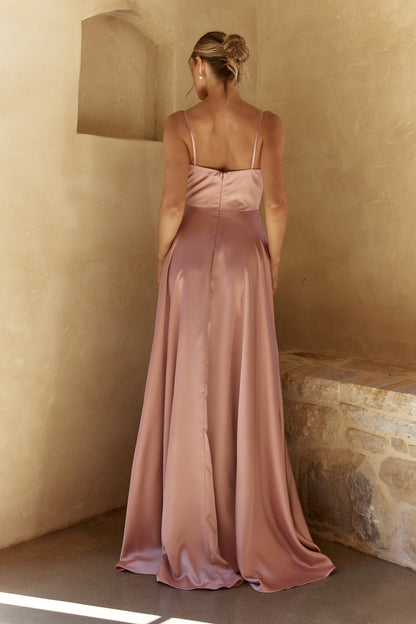 Woman in a pink evening gown standing against a beige wall.