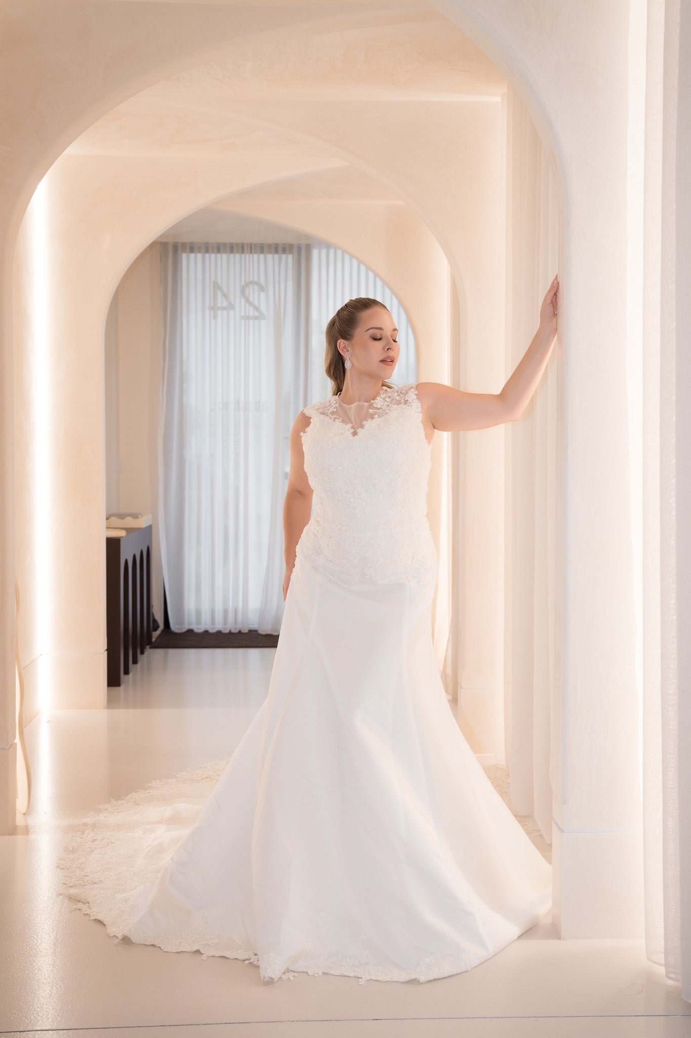 Woman in a white wedding dress standing in a softly lit room with arches.