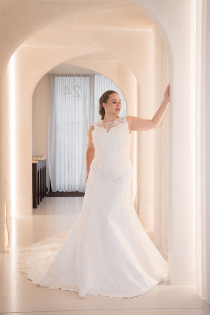 Woman in a white wedding dress standing in a softly lit room with arches.