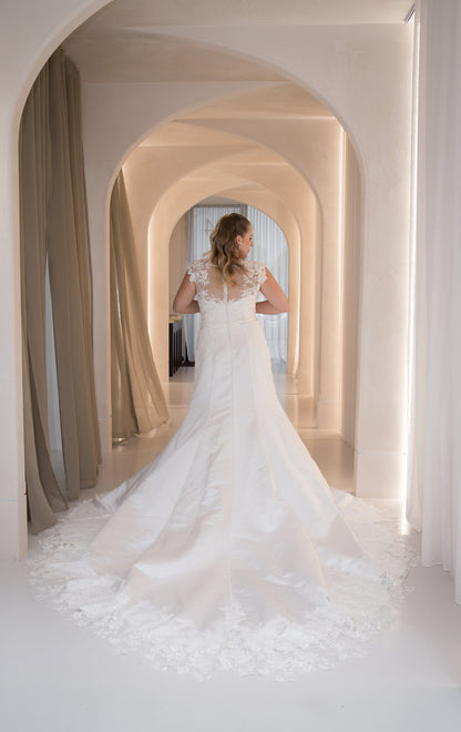 Woman in a white wedding dress standing in an elegant hallway with arches.