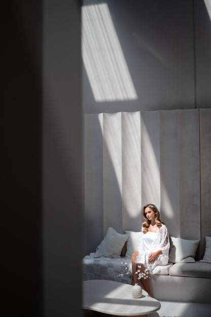 Woman sitting on a couch in a modern room with sunlight filtering through curtains