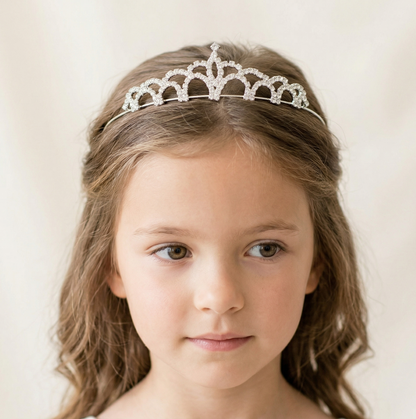Young girl wearing a silver tiara against a plain background