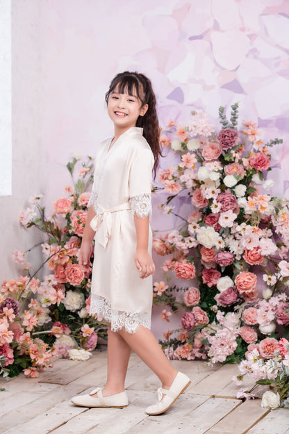 Young girl in a white dress standing in front of a floral arrangement with a light purple background