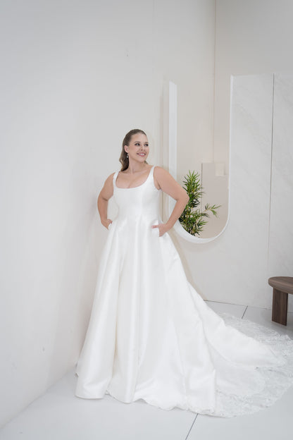Woman in a white wedding dress standing in a minimalistic room with a plant.