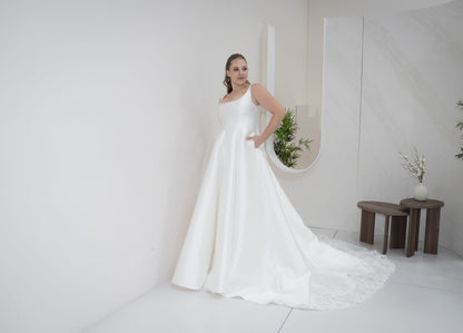 Woman in a white wedding dress standing in a minimalistic room with white walls and a small table.