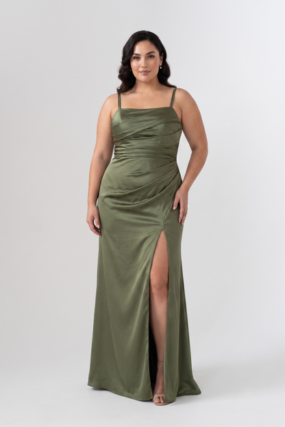 A woman modeling a floor-length olive green satin gown with spaghetti straps, a draped sweetheart neckline, and a high thigh slit, photographed against a light gray studio background.