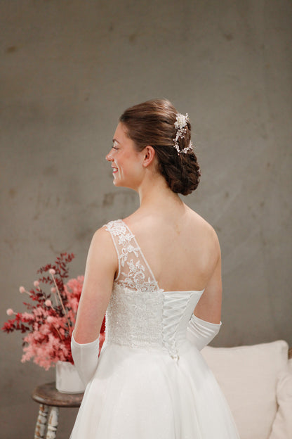Woman in a white wedding dress with lace detailing, standing against a neutral background.