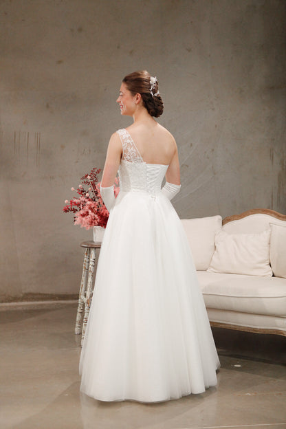 Woman in a white wedding dress holding flowers in a room with a couch and table.