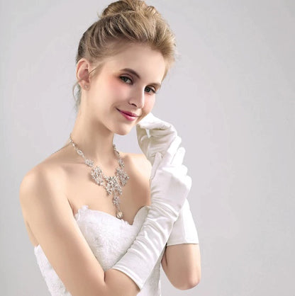 Woman wearing a white dress with a necklace and white gloves on a plain background