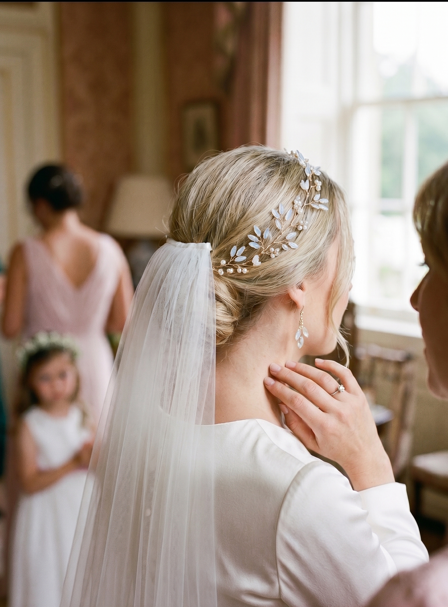 Bride with veil and decorative headpiece in a room with other people.