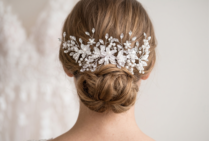 Woman with a styled hair bun wearing a delicate white hairpiece against a neutral background