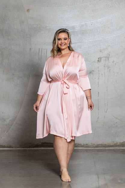 Woman wearing a pink satin robe against a gray concrete wall.