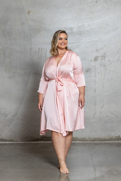 Woman wearing a pink satin robe against a gray concrete wall.