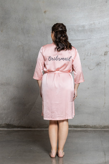 Person wearing a pink 'Bridesmaid' robe against a gray concrete wall