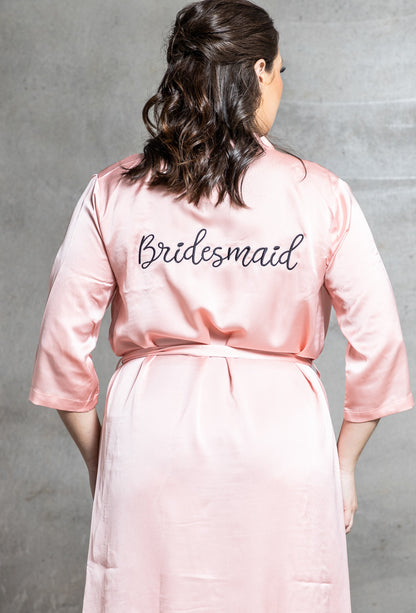 Person wearing a pink 'Bridesmaid' robe against a gray background