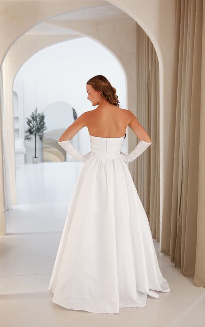Woman in a white strapless gown standing in a bright, arched room with neutral decor.