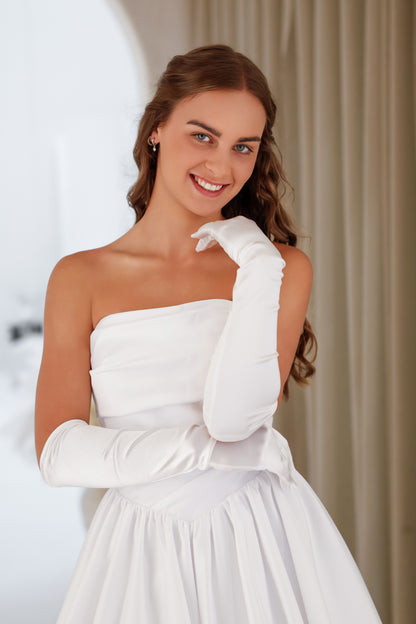 Woman in a white strapless dress with long white gloves posing against a neutral background