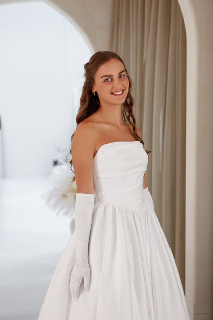 Woman in a white wedding dress with long gloves standing against a neutral background