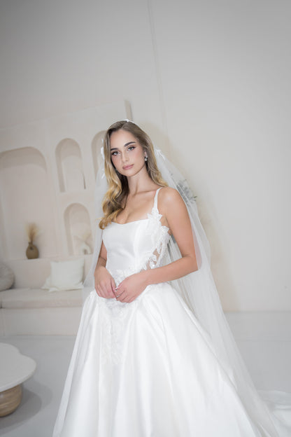 Woman in a white wedding dress with a long veil in a minimalistic room.