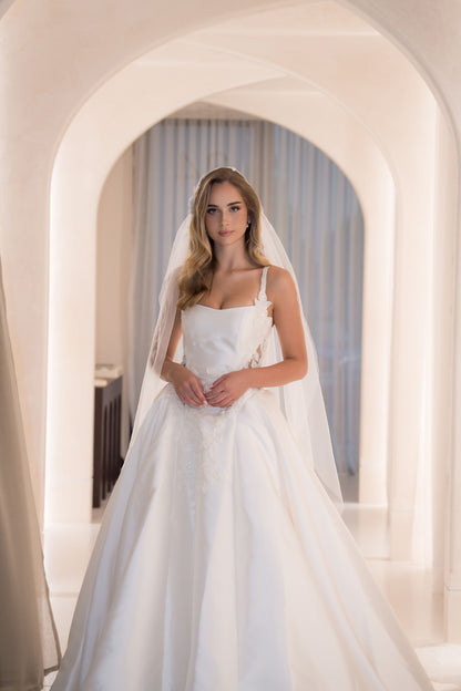 Woman in a white wedding dress standing in a softly lit hallway with arches.
