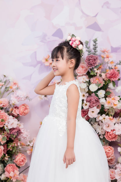 Young girl in a white dress standing in front of a floral arrangement with a light purple background