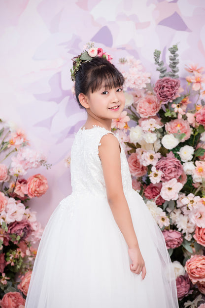 Young girl in a white dress standing in front of a floral backdrop