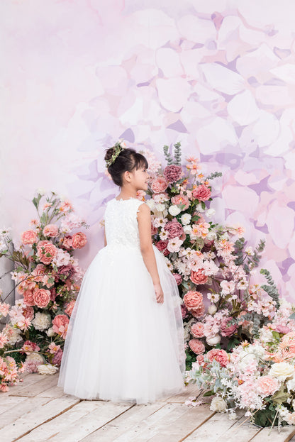 Woman in a white dress standing in front of a floral arrangement with a pastel butterfly backdrop.