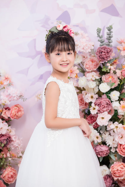 Young girl in a white dress standing in front of a floral backdrop